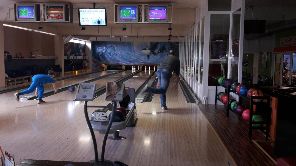 Hráč hádže bowlingovú guľu na osvetlenej dráhe.